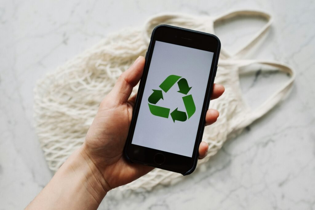 Main tenant un smartphone affichant un symbole de recyclage, posée sur un sac réutilisable, illustrant le numérique durable